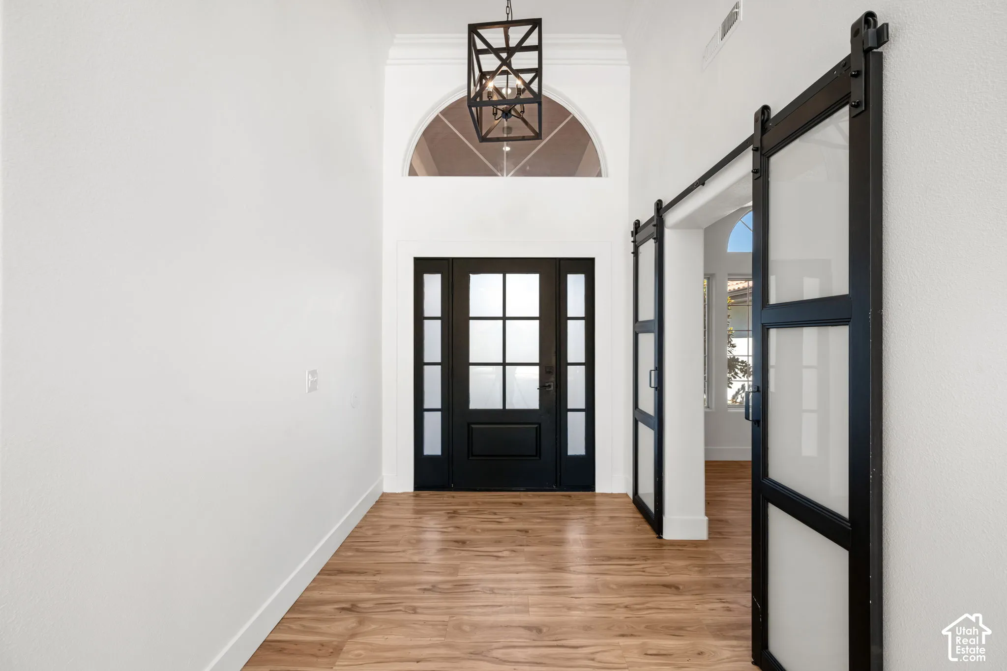 Entryway featuring a black double-door with frosted glass inserts, an arched transom window, a black metal chandelier, wood-finish flooring, and two frosted glass barn doors