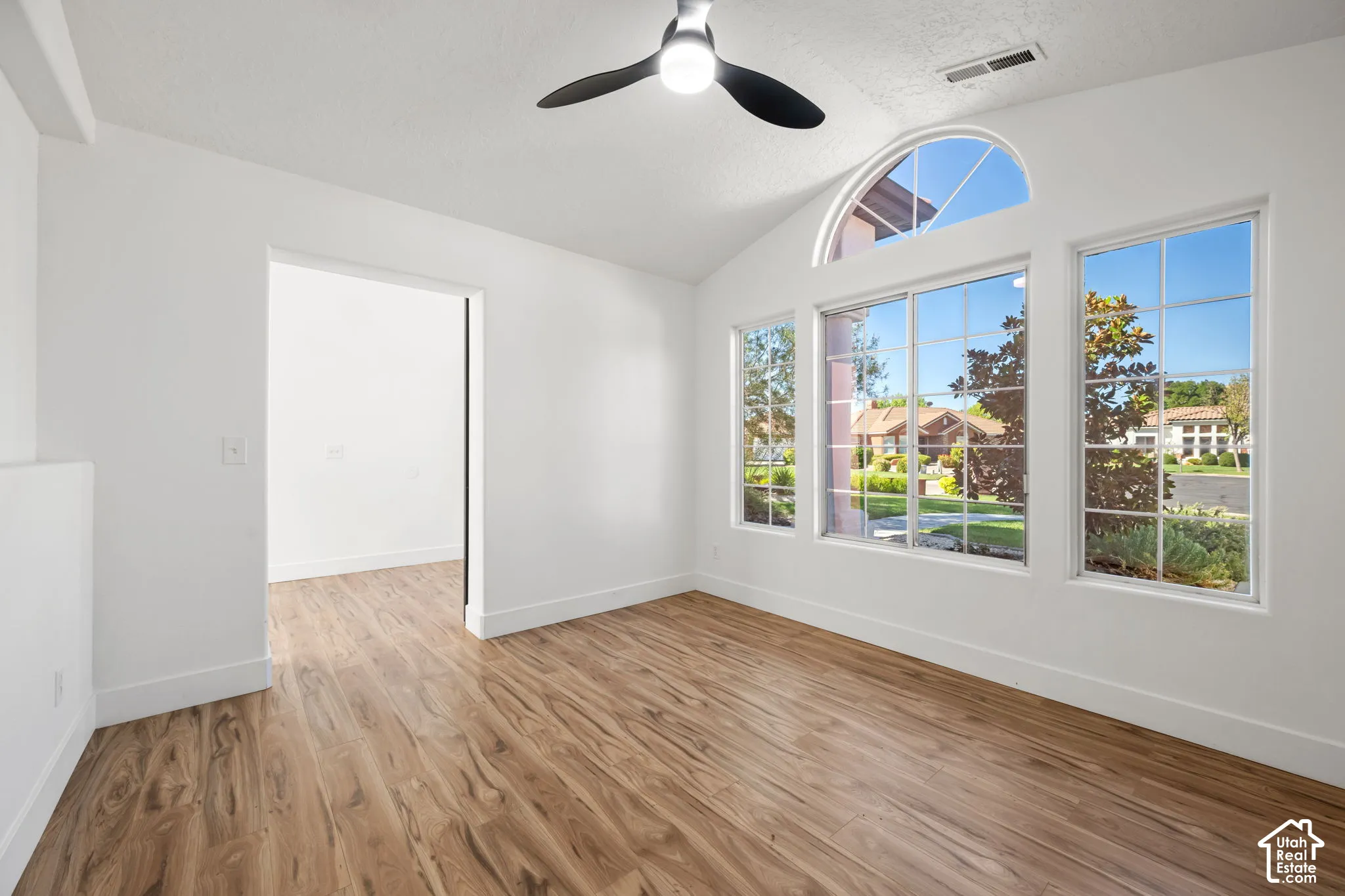 Vaulted ceiling with a ceiling fan, wood-finish flooring, and a large arched window