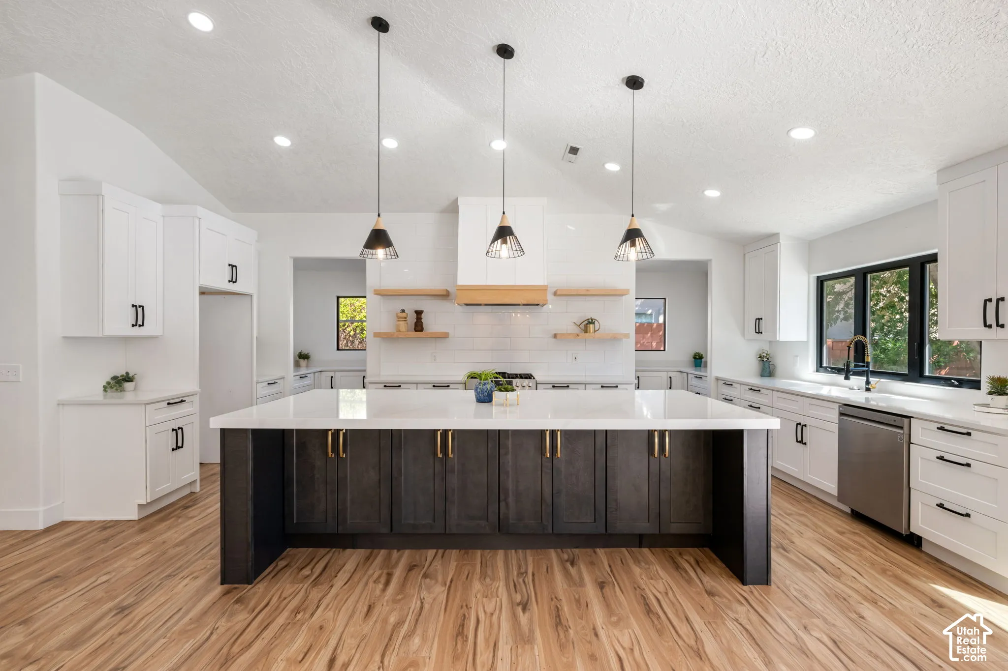Vaulted ceiling kitchen featuring an expansive center island, white cabinetry, wood-finish flooring, and pendant lighting