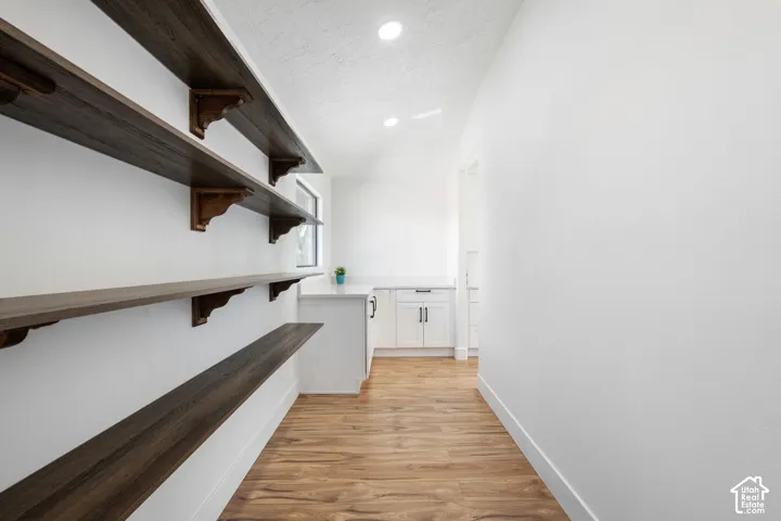 Wood-finish shelving with decorative brackets, light wood-finish flooring, recessed lighting, white cabinetry, and a countertop surface