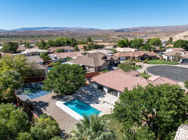 Outdoor swimming pool, fenced tennis court, mature trees, tiled roofing, and desert landscape backdrop