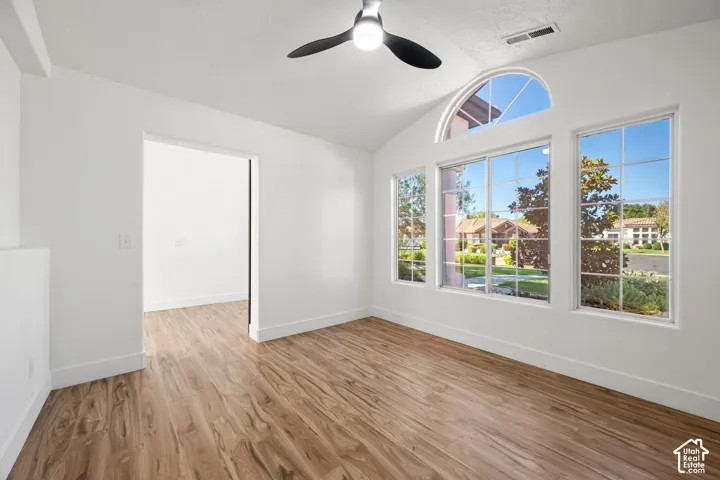 Vaulted ceiling with a ceiling fan, wood-finish flooring, and a large arched window