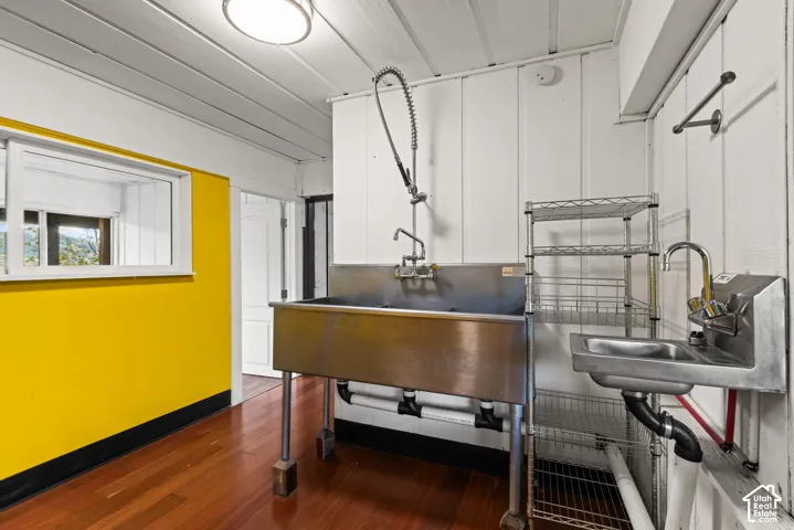 Hardwood flooring, stainless steel utility sink, additional stainless steel wall-mounted sink, white paneling, and a single window