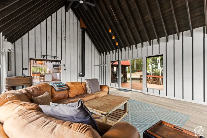 Vaulted wood-beamed ceiling, wood-finish flooring, sliding glass door to exterior deck, exposed stove pipe, and pass-through opening to kitchen