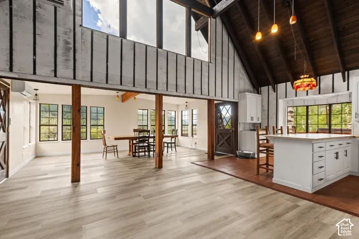 Vaulted wood-finish ceiling, large windows, wood-finish flooring, white kitchen cabinetry with island, and rustic wood beams