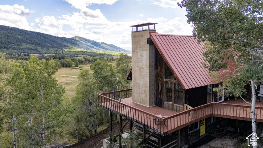 Structure with a red metal roof, a stucco chimney, and a wooden deck with railings