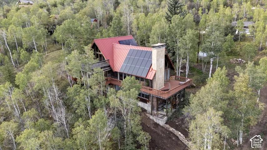 Red metal roof with solar panels, multiple exterior decks, and a prominent stone chimney