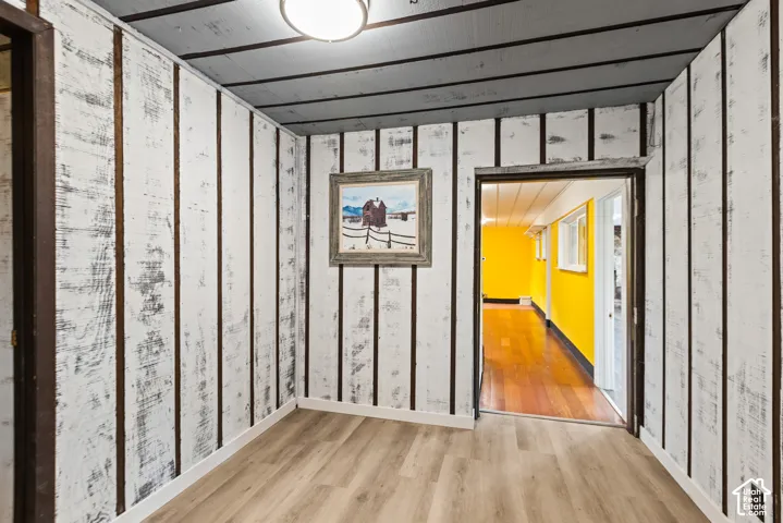 Wood-finish flooring with white baseboards, textured wood paneling, and an overhead flush-mount light fixture