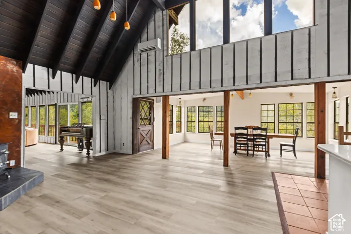 Vaulted wood-paneled ceiling, light wood-finish flooring, exposed wood beams, multiple large windows, and a built-in fireplace with a stone hearth