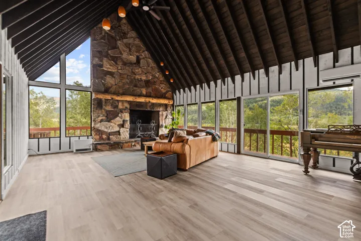 Vaulted wood-paneled ceiling, stone fireplace, wood-finish flooring, and expansive windows