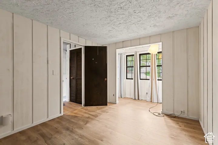 Wood-finish flooring, vertical paneling, two windows with dark frames, and a dark brown door