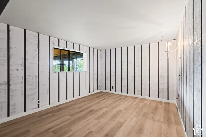 Wood-finish flooring, white board and batten style walls, single window with exterior view, and a wall-mounted sconce light fixture