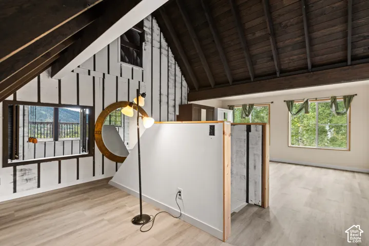 Vaulted wood-beam ceiling, wood-finish flooring, white and wood paneling, multiple windows, and natural light