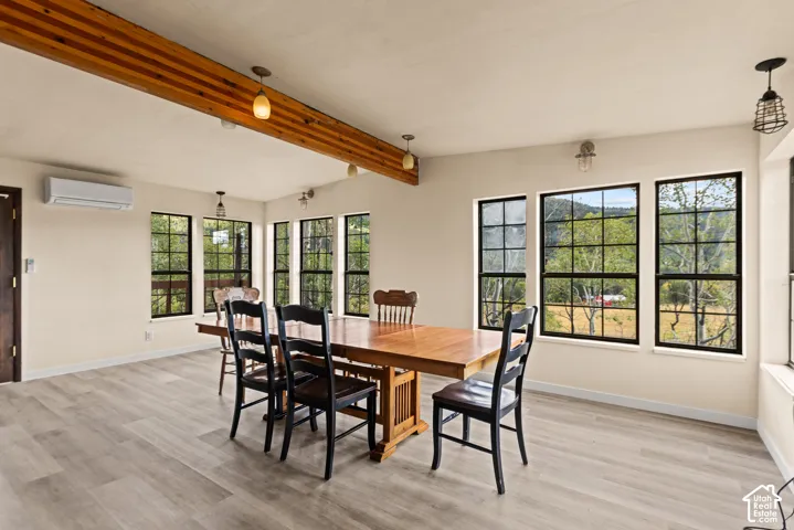 Spacious room featuring wood-finish flooring, exposed wood beam, multiple grid windows, and a wall-mounted climate control unit