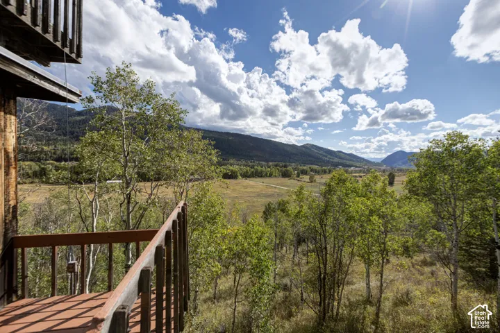 Wood deck with slat railing overlooking a expansive valley, mature deciduous trees, and distant mountains under a blue sky