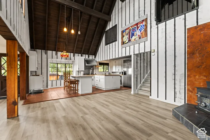 Vaulted wood-plank ceiling, wood-finish flooring, kitchen island with counter seating, built-in cabinetry, and a wood stove with a tiled hearth