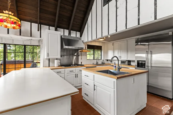 Vaulted wood-finish ceilings, white cabinetry with matte black hardware, stainless steel appliances, and butcher block countertops