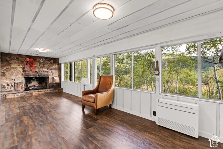 Floor-to-ceiling windows, stone-clad fireplace, wood-finish flooring, white paneled walls, and white beamed ceiling