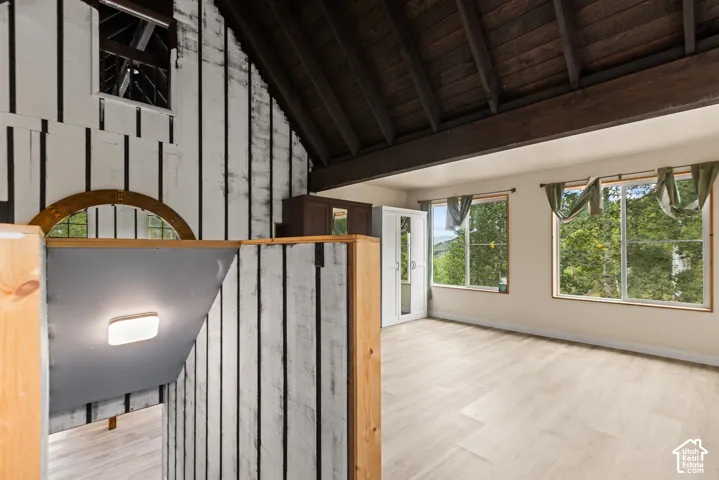 Vaulted wood-beam ceiling, light wood-finish flooring, multiple pane windows, and a built-in arch window feature