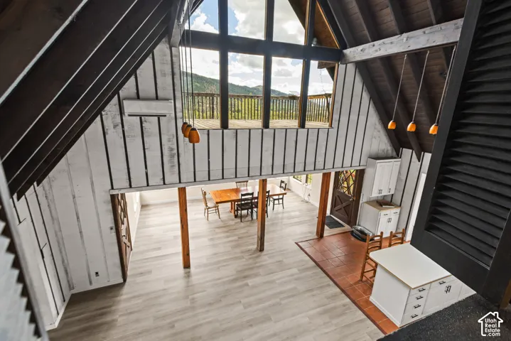 Vaulted ceilings with exposed beams, wood-finish flooring, a built-in kitchen island, white cabinetry, and a balcony with wooden railings