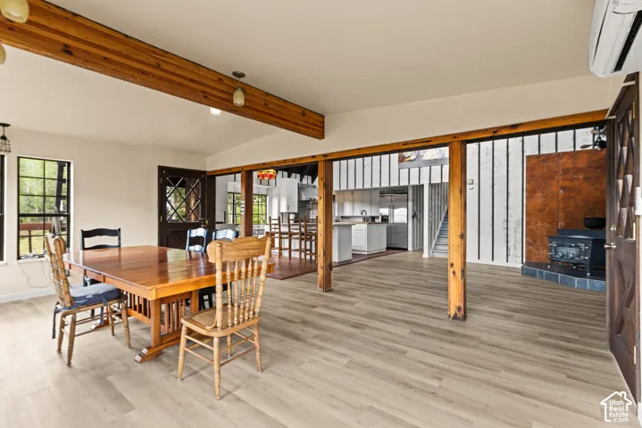 Open-concept living space with exposed wood beams, wood-finish flooring, a built-in wood stove, and a decorative paneled door