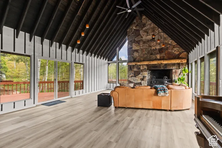 Vaulted wood-paneled ceiling with exposed beams, large stone fireplace with a wood mantle, wood-finish flooring, and multiple sliding glass doors leading to an exterior deck