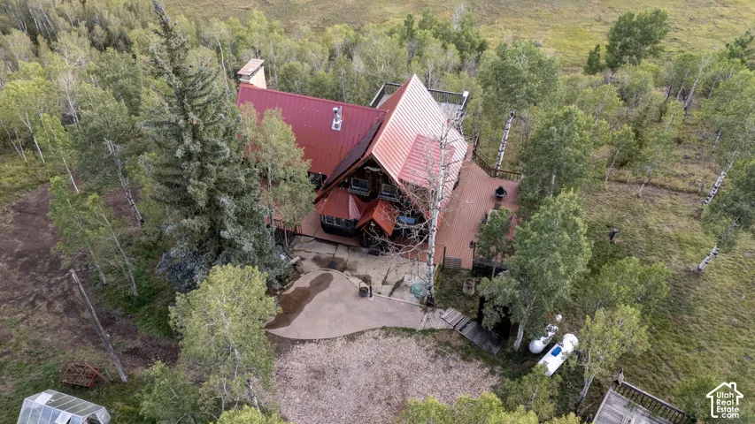 Red metal roof, expansive outdoor decking, surrounding mature trees, concrete patio, and a rustic exterior finish