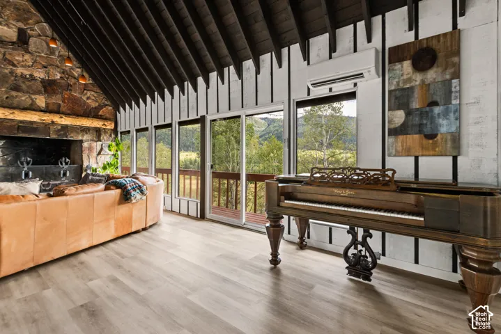 Vaulted wood-paneled ceiling, stone-clad fireplace with wood mantel, light wood-finish flooring, and multiple sliding glass doors leading to an exterior deck