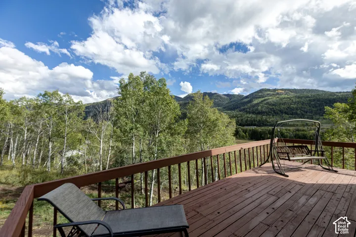 Expansive outdoor deck with wood flooring and a perimeter railing, overlooking a mountainous landscape with abundant tree coverage