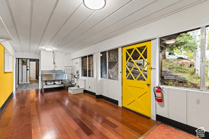 Hardwood flooring, white paneled ceilings, stainless steel utility sink, multiple windows, and a vibrant yellow door