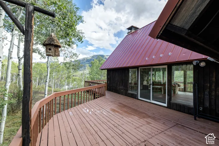 Expansive deck with wood-finish railing, a red metal roof, and large glass sliding doors