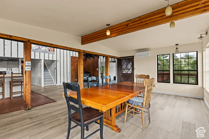 Open concept living space featuring light wood-finish flooring, exposed wood beams, multiple windows, and an exposed wood door