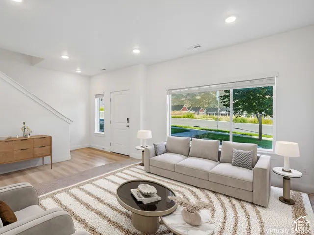 Recessed ceiling lighting, large picture window with blinds, wood-finish flooring, white painted walls, and a white interior door