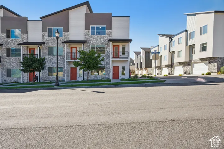 Modern townhome exterior featuring stone and siding finishes, a prominent red entry door, a balcony, and a two-car garage