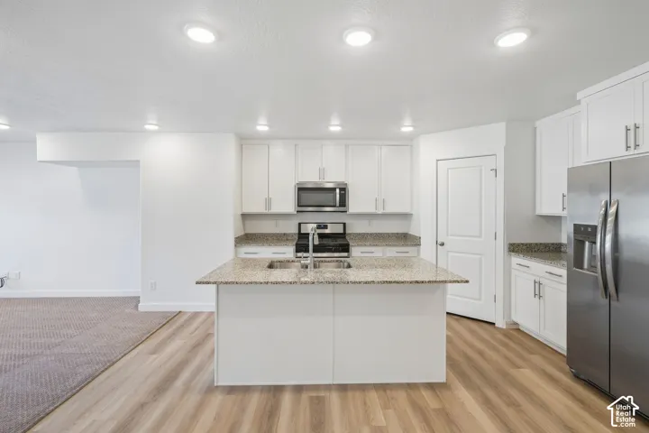Kitchen featuring a central island, stainless steel appliances, white cabinetry, and wood-finish flooring