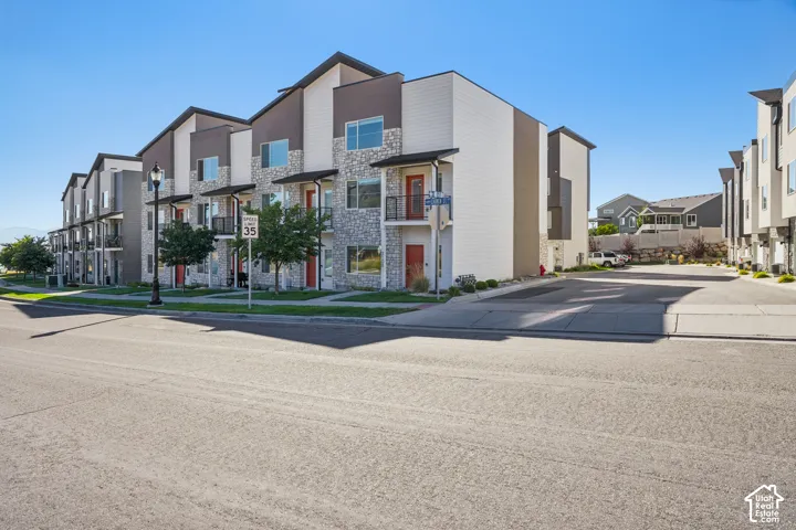 Contemporary townhome exterior featuring stone accents, multi-level design, individual balconies, and a paved parking area