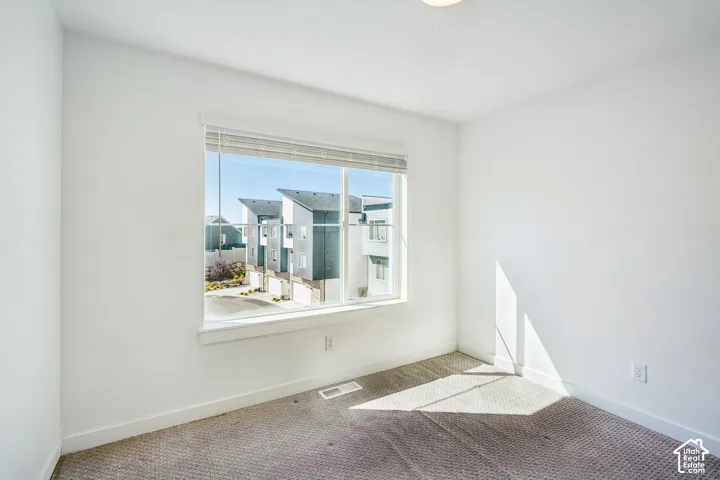 White walls and gray carpeting, featuring a large window with blinds