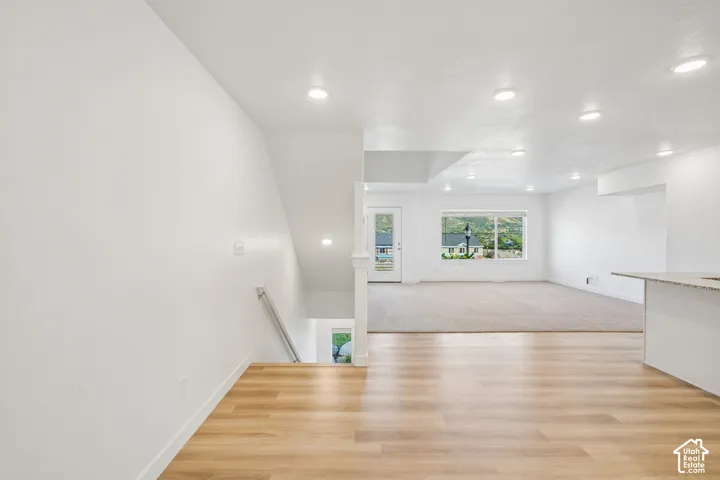 Wood-finish flooring, recessed lighting, white walls, and a staircase with a white railing