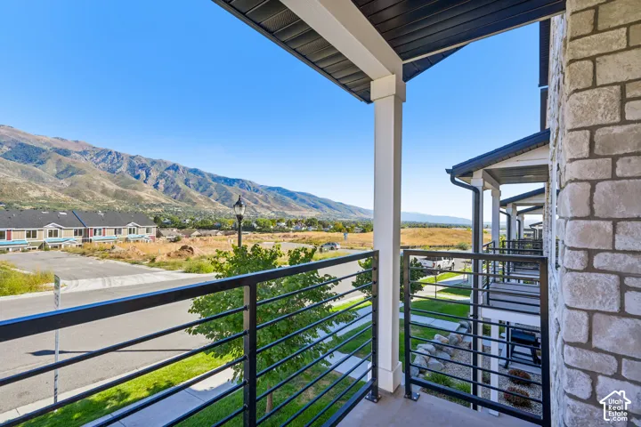 Balcony with black metal railings, white columns, mountain scenery, and stone exterior