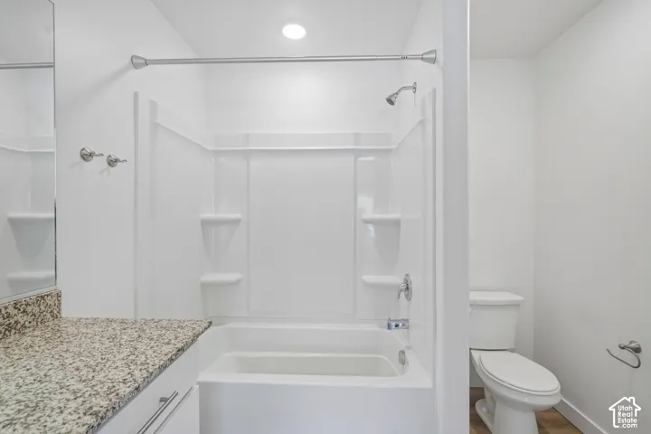 Bathroom featuring a combined shower and tub, granite-finish countertop, and a white toilet