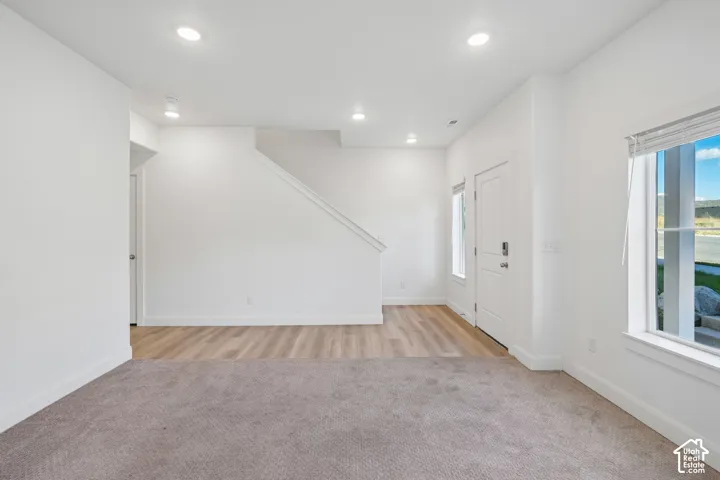 Recessed ceiling lighting, wood-finish flooring, staircase with white railing, white interior door, and window with blinds