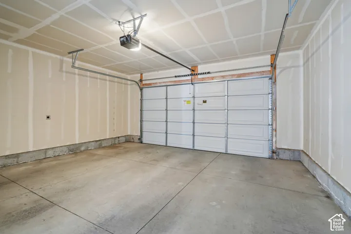 Concrete flooring, automatic garage door opener, white paneled garage door, exposed ceiling joists, light-colored walls