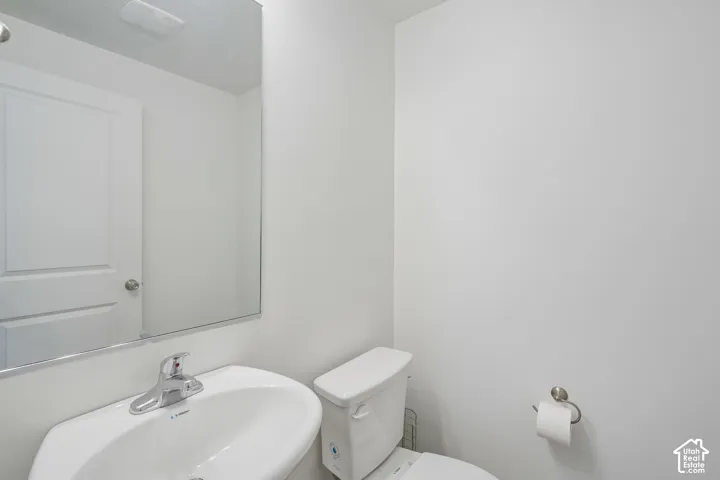 Pedestal sink with chrome faucet, wall-mounted mirror, and white toilet