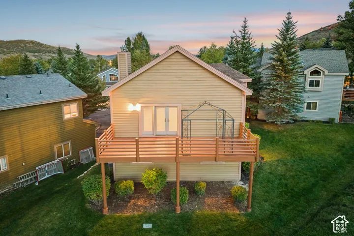 Elevated wood-finish deck with horizontal slat railings, featuring double glass doors, exterior wall lighting, and a manicured lawn