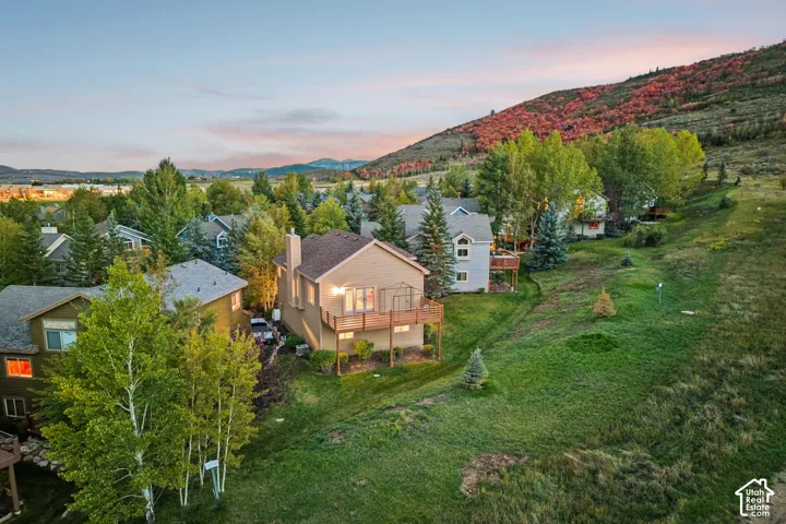 Terraced hillside property with mature trees, a multi-level deck, and a sloping green lawn
