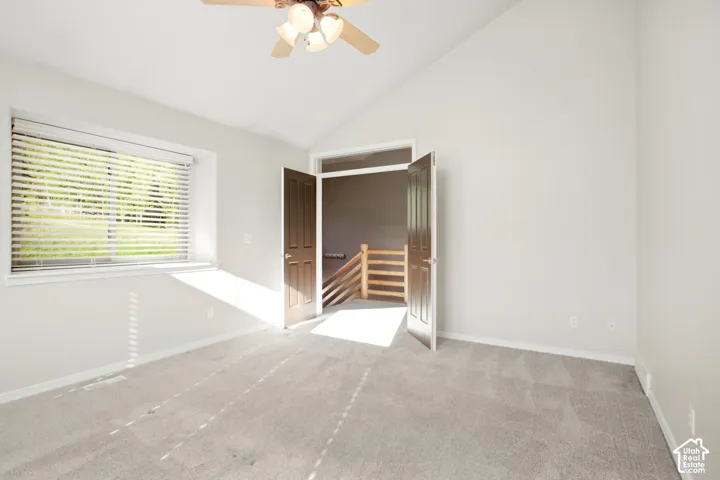 Vaulted ceiling, ceiling fan with integrated lighting, carpeted flooring, window with blinds, and double panel doors