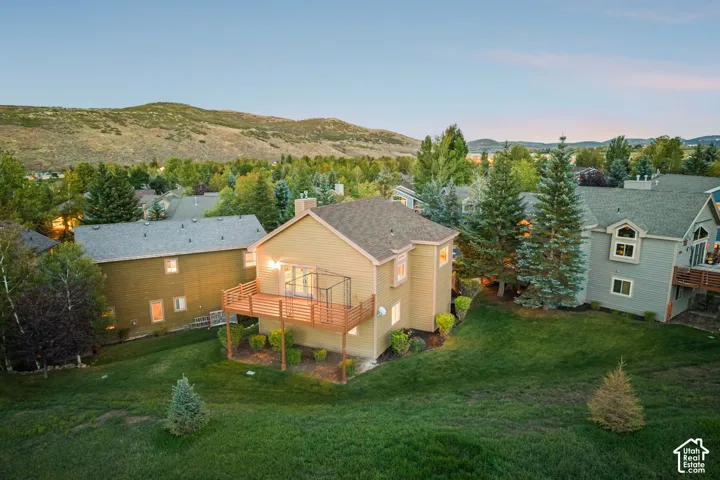 Expansive green lawn with mature trees, multi-level dwelling with a gabled roof, and a wood-finish deck with railing