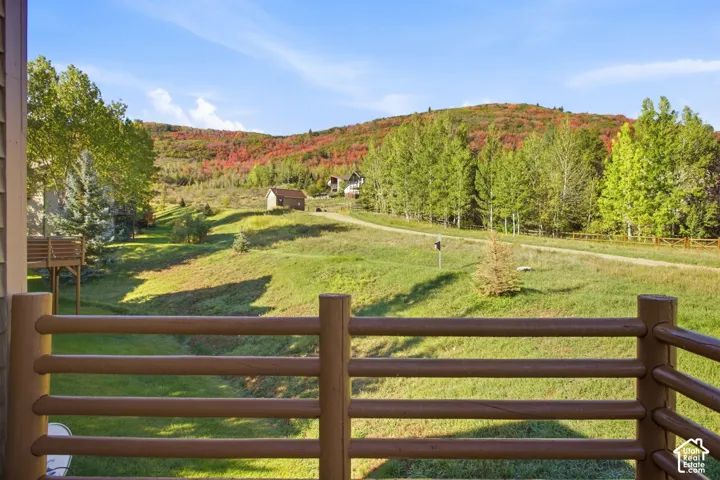 Expansive natural landscape with rolling hills, distant trees displaying autumn foliage, and a rustic log railing