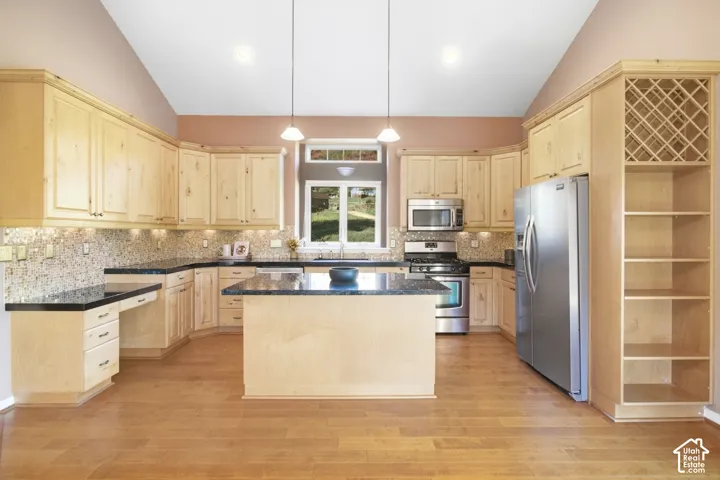 Vaulted ceiling kitchen featuring wood-finish flooring, light wood cabinetry, stone countertops, and stainless steel appliances