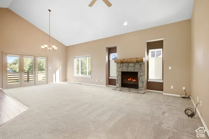 Vaulted ceiling with an attached chandelier, stone fireplace with a wood mantle, and sliding glass doors